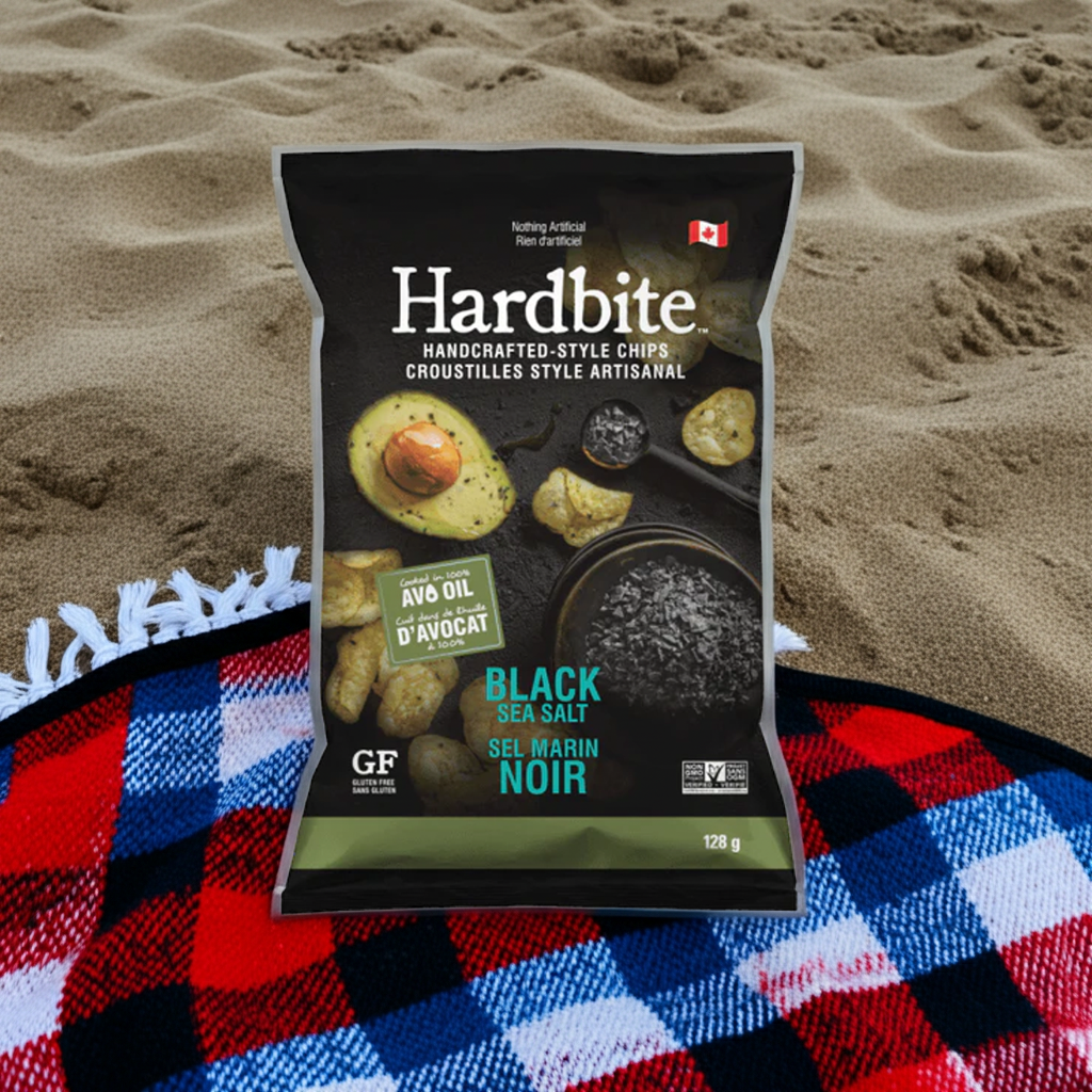 Hardbite black sea salt chips packaging on a beach with sand and a blanket.