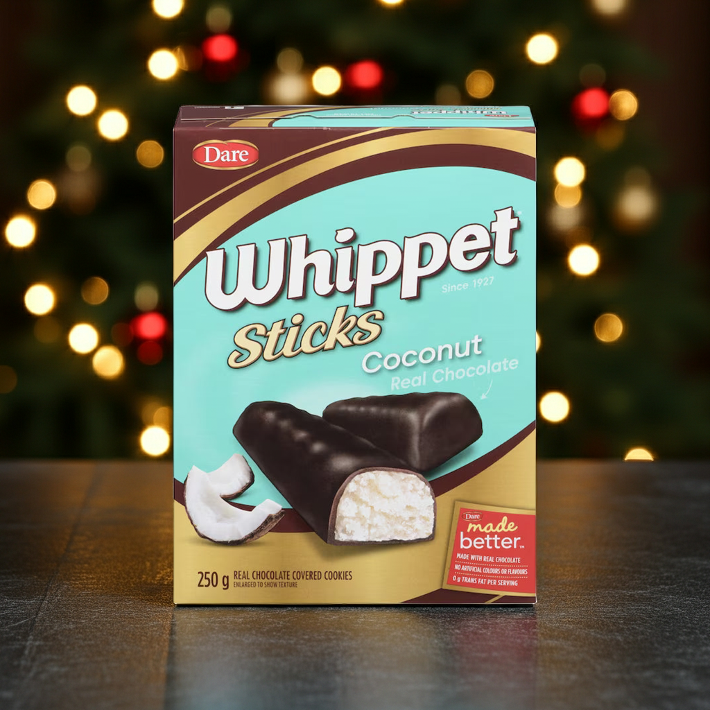 A box of Dare Whippet Sticks Coconut Red Chocolate cookies stands on a dark tabletop with a blurred Christmas tree and warm bokeh lights in the background.